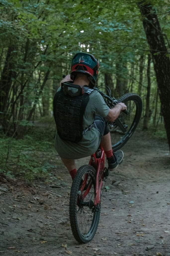 A mountain biker performs a wheelie on a forest trail, showcasing skill and adventure.