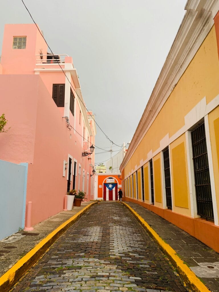 pexels-photo-14625211-14625211 Charming narrow street in Old San Juan flanked by colorful buildings with the Puerto Rican flag.
