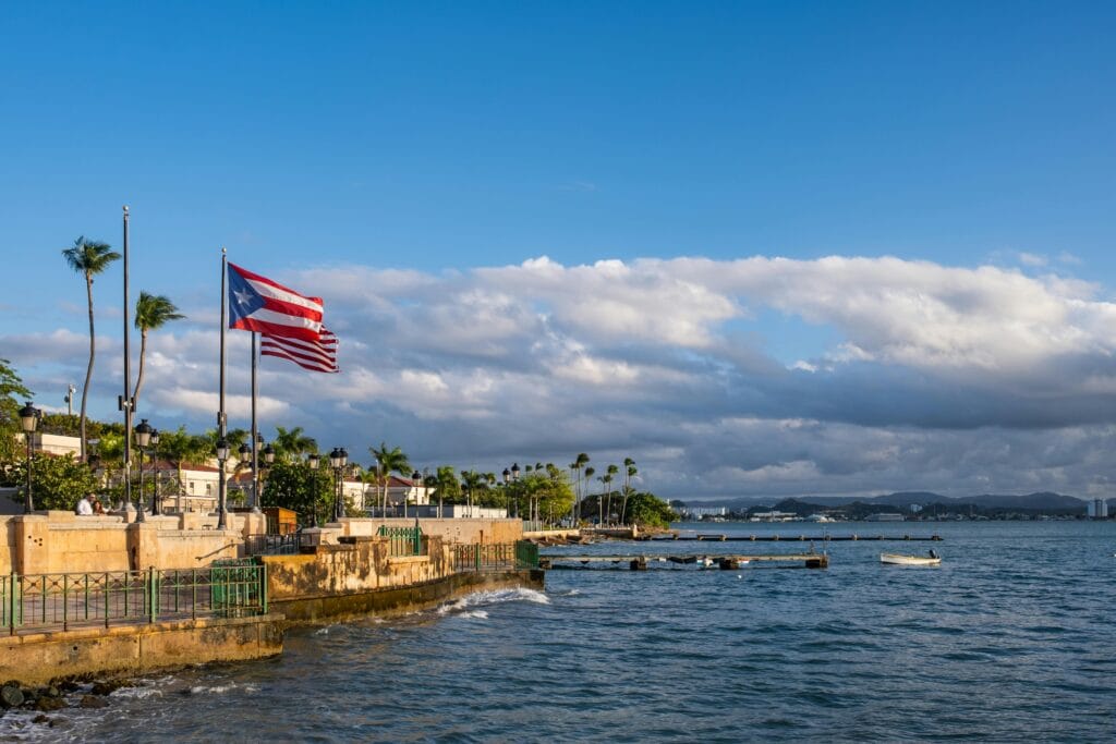 A picturesque view of the Puerto Rican waterfront with a flag waving against a backdrop of the sea and cityscape.