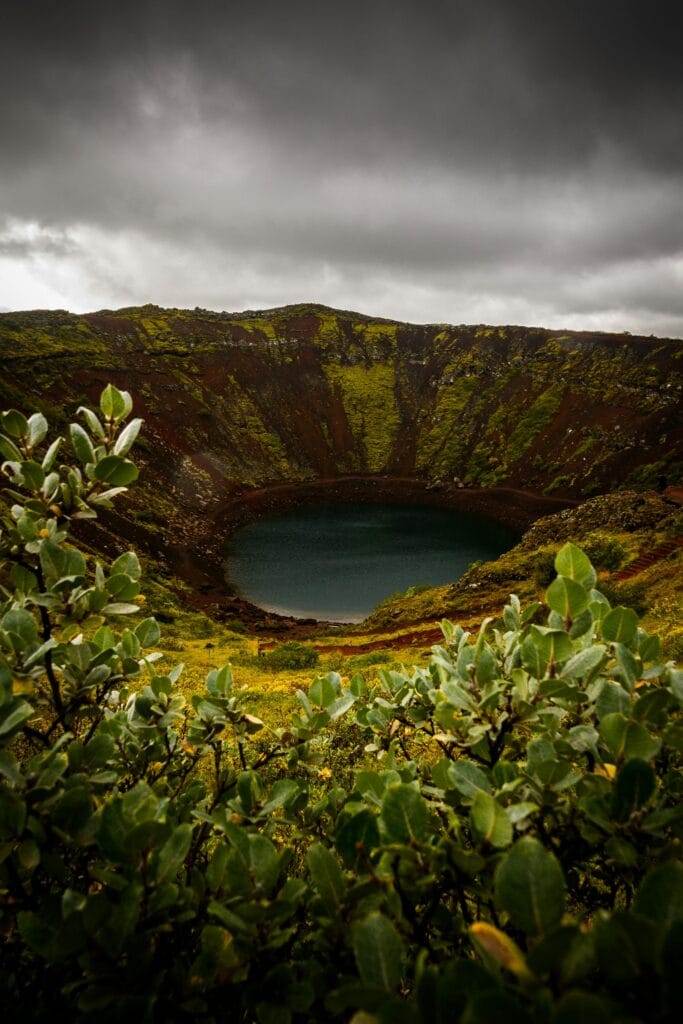 Explore the dramatic landscape of Kerid Crater Lake surrounded by lush greenery under moody skies.