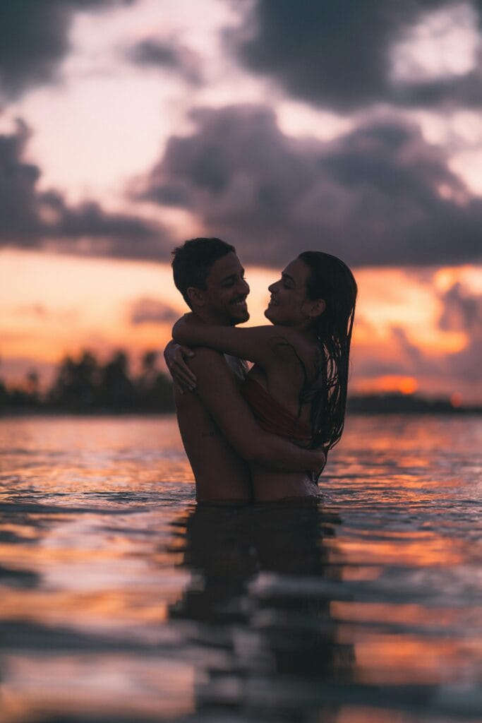 A romantic couple embracing in the ocean with a dramatic sunset in Barra Grande, Brazil.