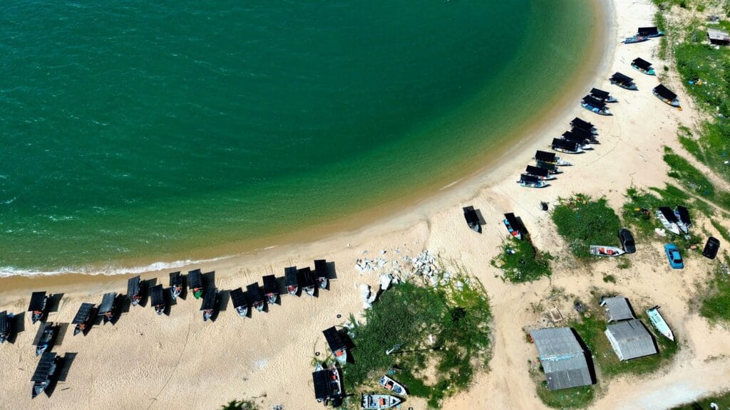 A stunning aerial view shows boats lined up on a serene sandy beach, beside clear turquoise water.