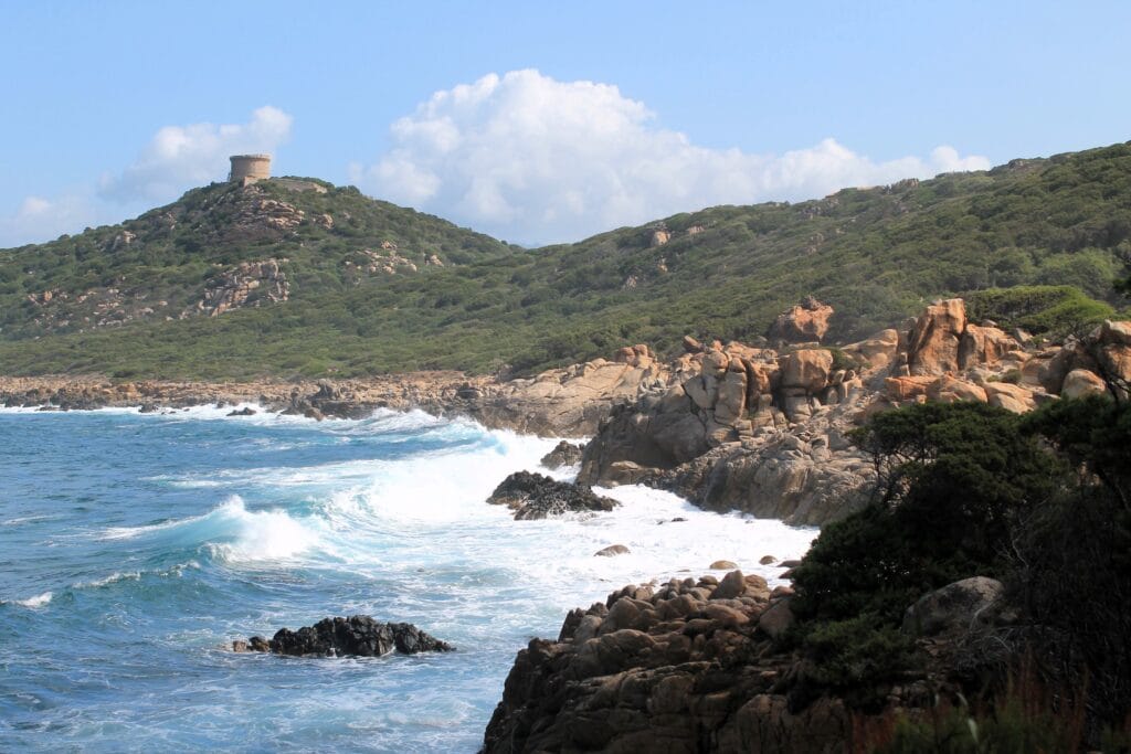 Scenic view of rugged coastline with waves crashing against rocks and a distant historic tower.