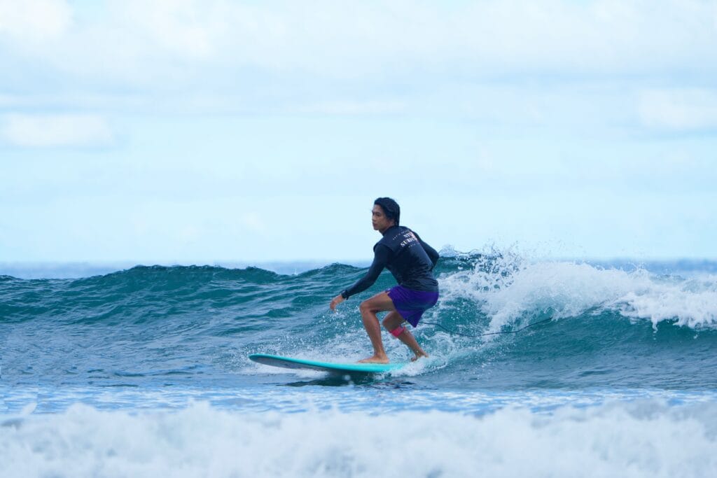 A teenager skillfully surfs a wave on a bright summer day by the sea.