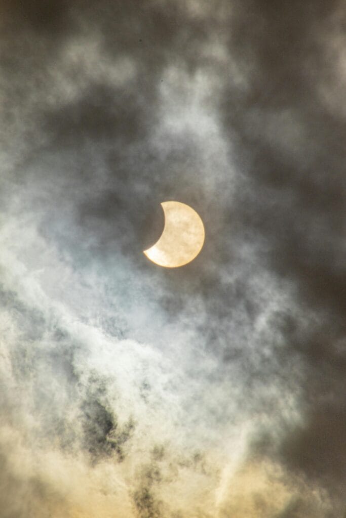 A captivating view of a solar eclipse partially covered by clouds in the sky.